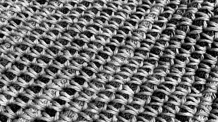 a black and white photo of crochet piece where cotton yarn is wrapped around a bigger yarn
